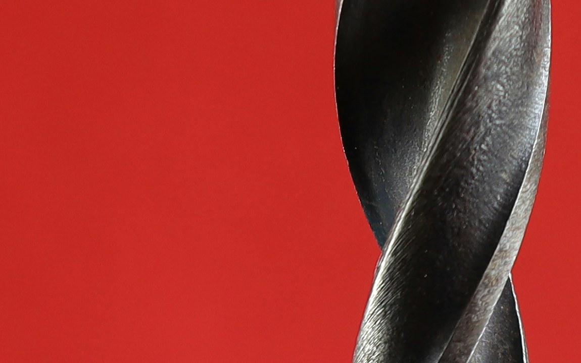 Macro shot of a twisted metal drill bit against a red background