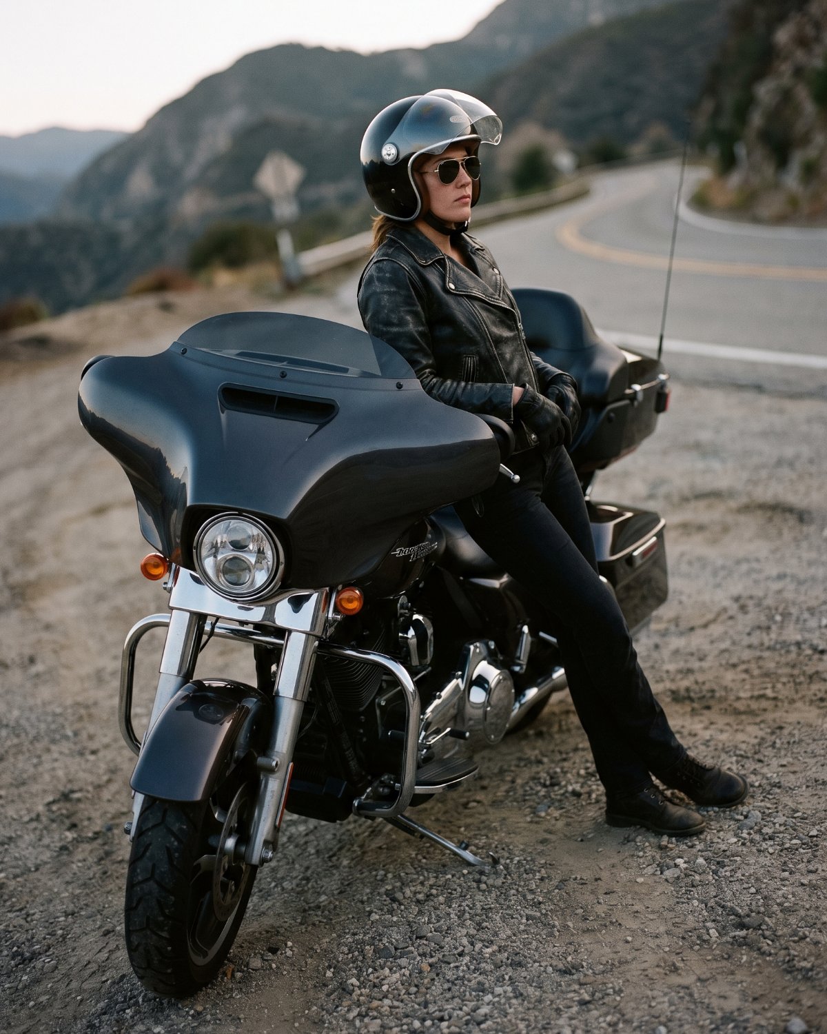 A rider in leather gear and a helmet seated on a Harley-Davidson touring motorcycle on a mountain road