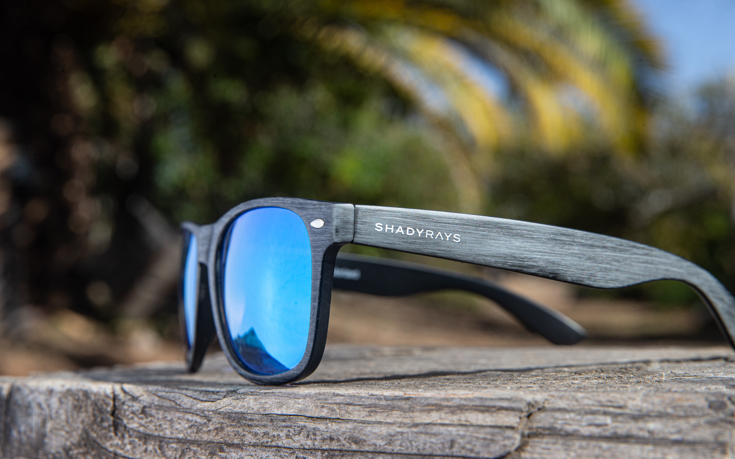Shady Rays polarized sunglasses, blue mirrored lenses, shot outdoors on a wooden ledge