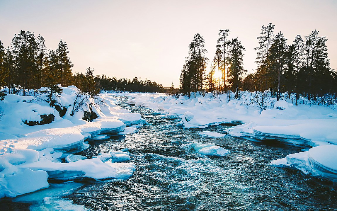 Frozen river running through a snow-covered Nordic forest at sunset